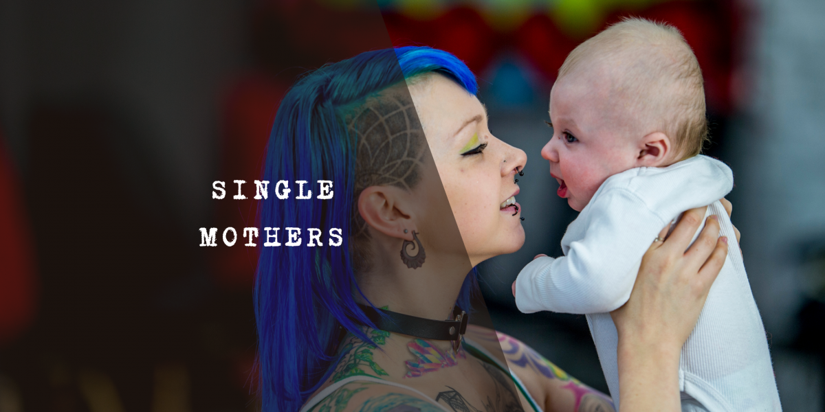 A mum with blue hair holding and looking at a baby.