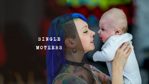 A mum with blue hair holding and looking at a baby.