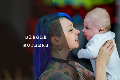 A mum with blue hair holding and looking at a baby.